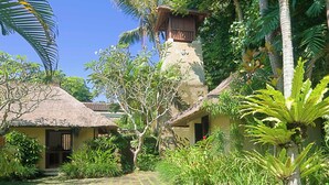 A tropical resort with thatched-roof huts, lush greenery, and a central stone structure. - Villa Alamanda (Ubud)
