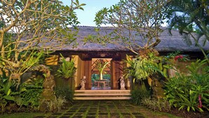 A traditional thatched-roof structure with a stone pathway leading to a seating area. - Villa Alamanda (Ubud)