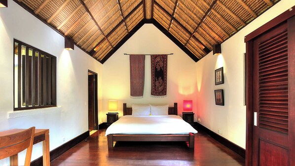 A hotel room with a bed, a wooden chair, a window with bars, a door, and a ceiling with a woven pattern.