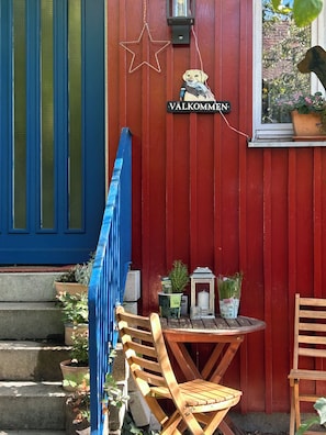 A red wooden wall with a sign reading 'VÄLKOMMEN' and a star decoration. There is a small table with chairs, a lantern, and potted plants. - Close! Schwaig Vacation Apartment (Schwaig bei Nürnberg)