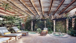 A covered outdoor area with lounge chairs, a small pool, and a stone wall.