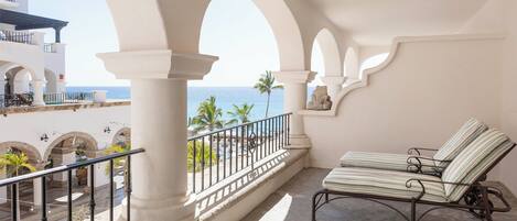 A balcony with a sun lounger, white columns, and a view of the sea.