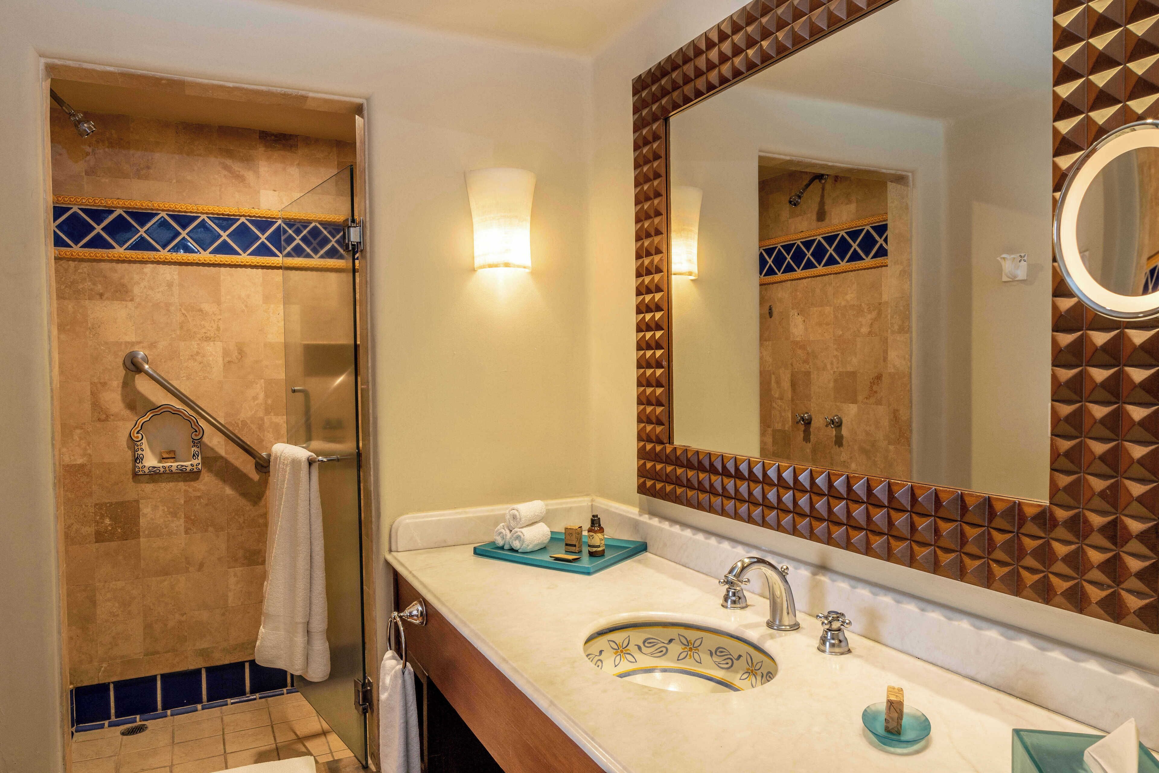 A bathroom with a glass shower, a sink with a decorative basin, and a large mirror with a geometric tile backsplash.
