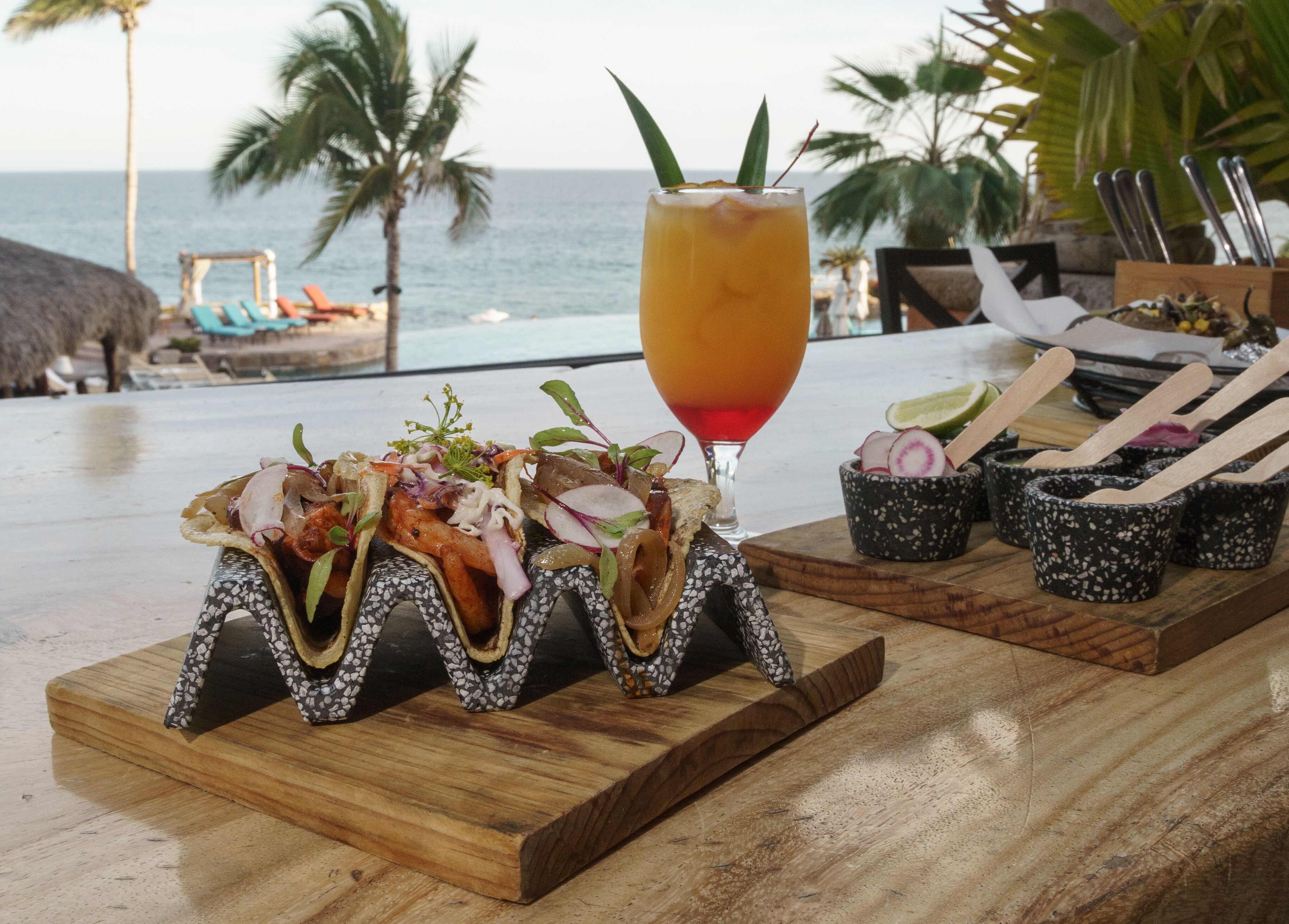 A wooden table with a seafood appetizer, a cocktail, and a small dish with wooden utensils.