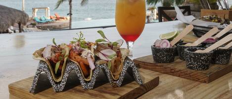 A wooden table with a seafood appetizer, a cocktail, and a small dish with wooden utensils.