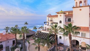 A coastal hotel with multiple balconies, palm trees, and a view of the ocean.