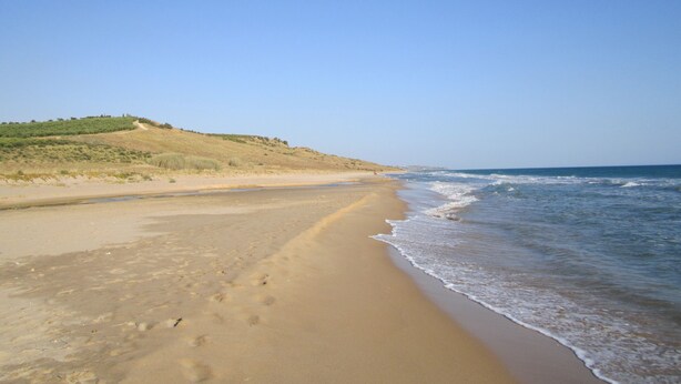 A wide sandy beach with gentle waves, a clear sky, and a hill with sparse vegetation in the background. - Gioberta Holiday Homes, Cipollazzo Villa (Menfi)