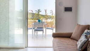 A room with a sliding glass door leading to an outdoor patio with a table and chairs, a beige sofa, and a wall-mounted thermostat. - Gioberta Holiday Homes, Cipollazzo Villa (Menfi)