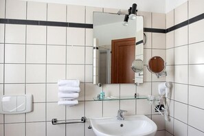 Een badkamer met een wit wastafel, twee spiegels, een handdoekhouder en een glazen plank.