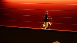 A dimly lit room with a red wall, a bottle of wine, and two glasses on a shelf. - Room in Guest Room - Alba Village Hotel Room Twin Beds (Alba)