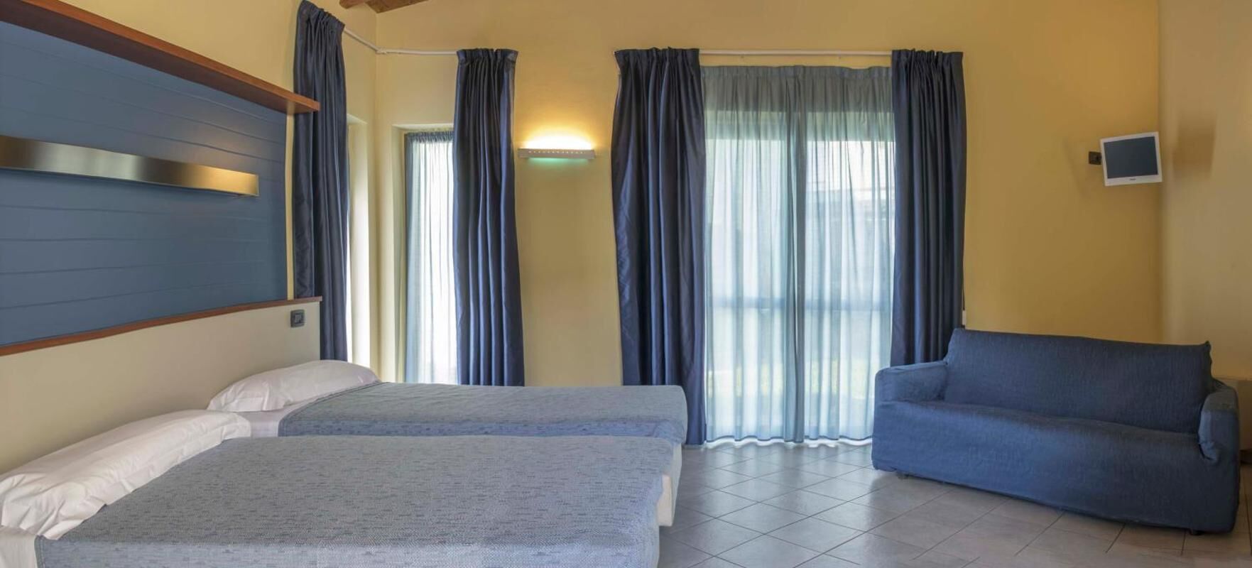 Une chambre avec deux lits, un canapé, une télévision et une fenêtre avec des rideaux.
