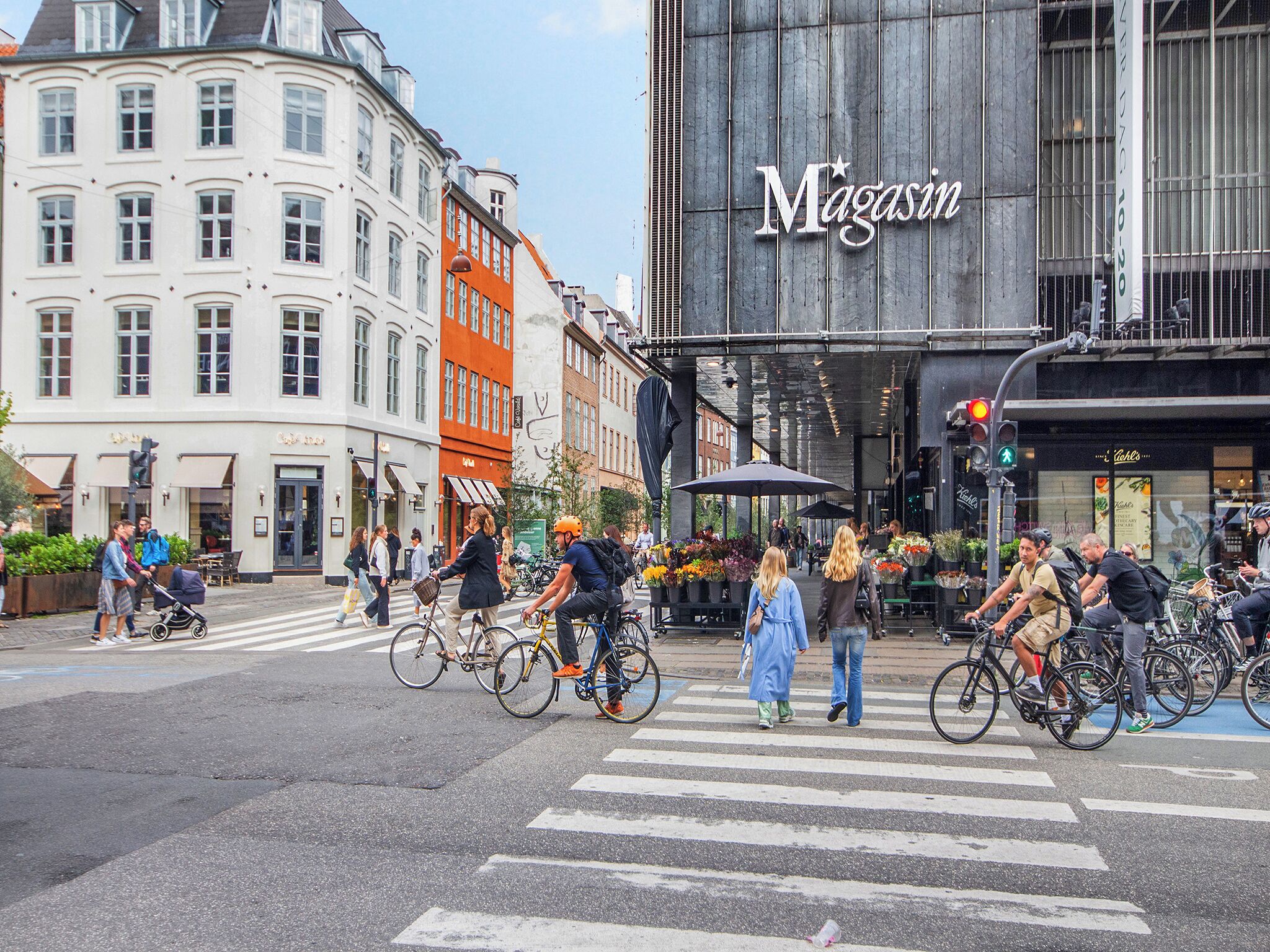 Straßenszene mit Fußgängerüberweg, Gebäuden und einem großen Schild mit der Aufschrift 'Magasin'.