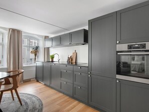 A modern kitchen with grey cabinetry, a wooden dining table, and a window with curtains. - Regent 4- Cute 1-bdr Apt in Centre of Copenhagen (Copenhagen)