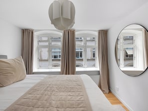 A bedroom with a large bed, two windows with curtains, a round mirror, and a ceiling light fixture. - Regent 4- Cute 1-bdr Apt in Centre of Copenhagen (Copenhagen)