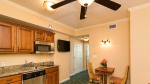 A kitchen with wooden cabinets, a microwave, and a dishwasher. There is a dining area with a table and chairs, and a ceiling fan. - Westgate Myrtle Beach Oceanfront 828-94 (Myrtle Beach)