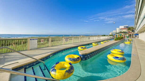 A pool with yellow and blue inflatable rings, a lifeguard stand, and a view of the ocean. - Westgate Myrtle Beach Oceanfront 828-94 (Myrtle Beach)