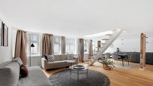 Un salon moderne avec un canapé gris, une table basse ronde et un coin repas comprenant une table et des chaises.