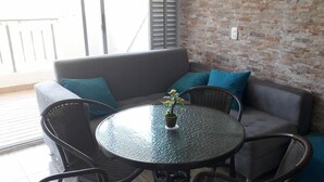 Un espace extérieur accueillant avec une table ronde en verre, des chaises en osier et un canapé gris agrémenté de coussins turquoise.
