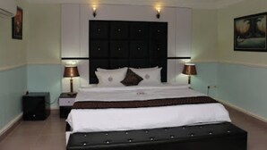 A hotel room with a large bed, two bedside lamps, a black headboard, and a painting on the wall. - Room-all Seasons Hotel - Business Suite (Owerri)