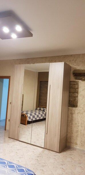 Un dormitorio con un armario grande, una cama con ropa de cama estampada y una pared de piedra.