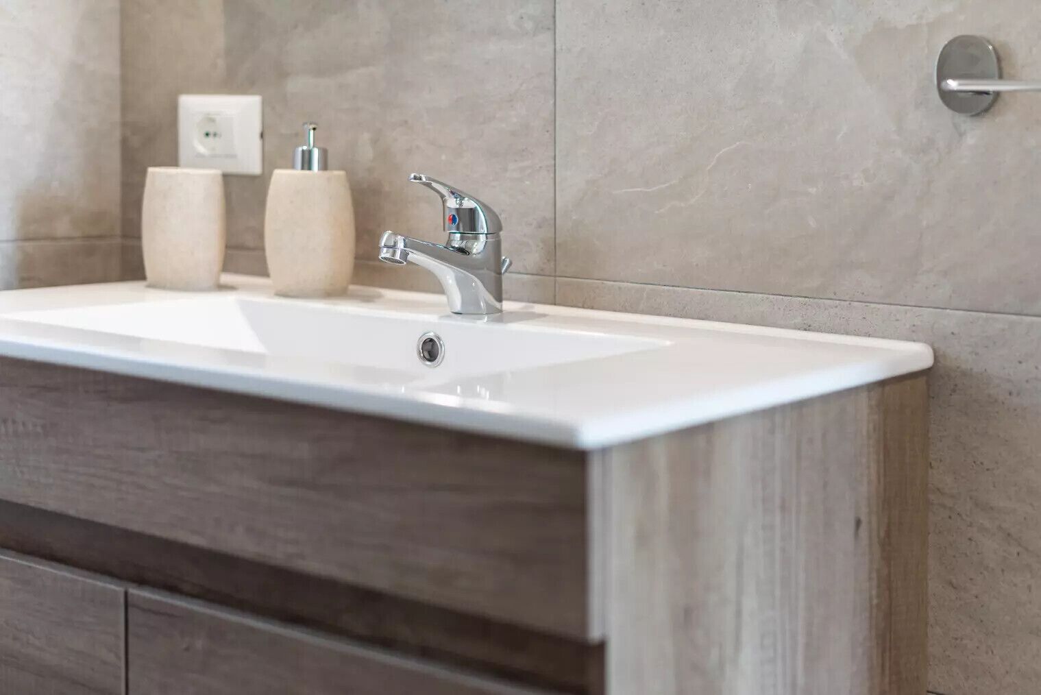 A bathroom with a white sink, a modern faucet, and wooden cabinetry.