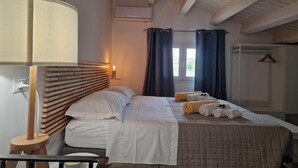 Une chambre avec une tête de lit en bois, une lampe de chevet, un lit avec une literie blanche et marron, une fenêtre avec des rideaux et un porte-manteau suspendu.