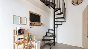 Un escalier avec une rampe en métal noir, une étagère en bois contenant divers objets, un réfrigérateur blanc et une horloge au mur.