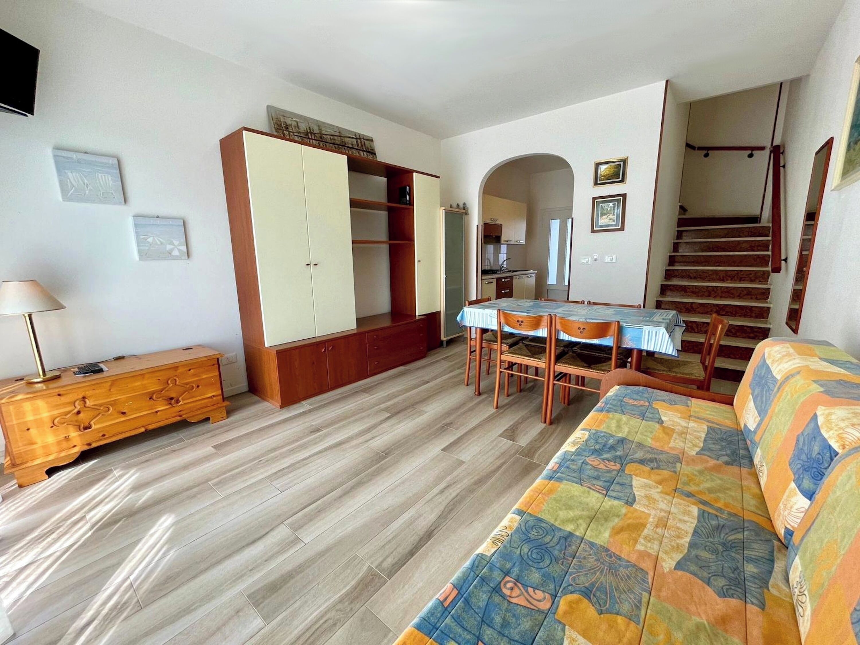 A living room with a sofa, a wooden cabinet, a dining table with chairs, and a staircase.