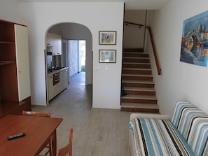 Un salon avec un canapé, une table à manger en bois et une télécommande posée dessus. Un escalier mène à une autre pièce.