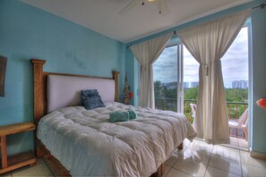 Relax in this serene bedroom with a large bed and balcony offering views of the surrounding area.