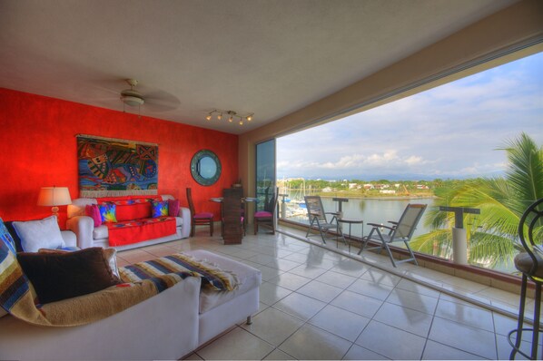 Relax in this stylish living area with a scenic view of the water and palm trees from the large window and balcony.