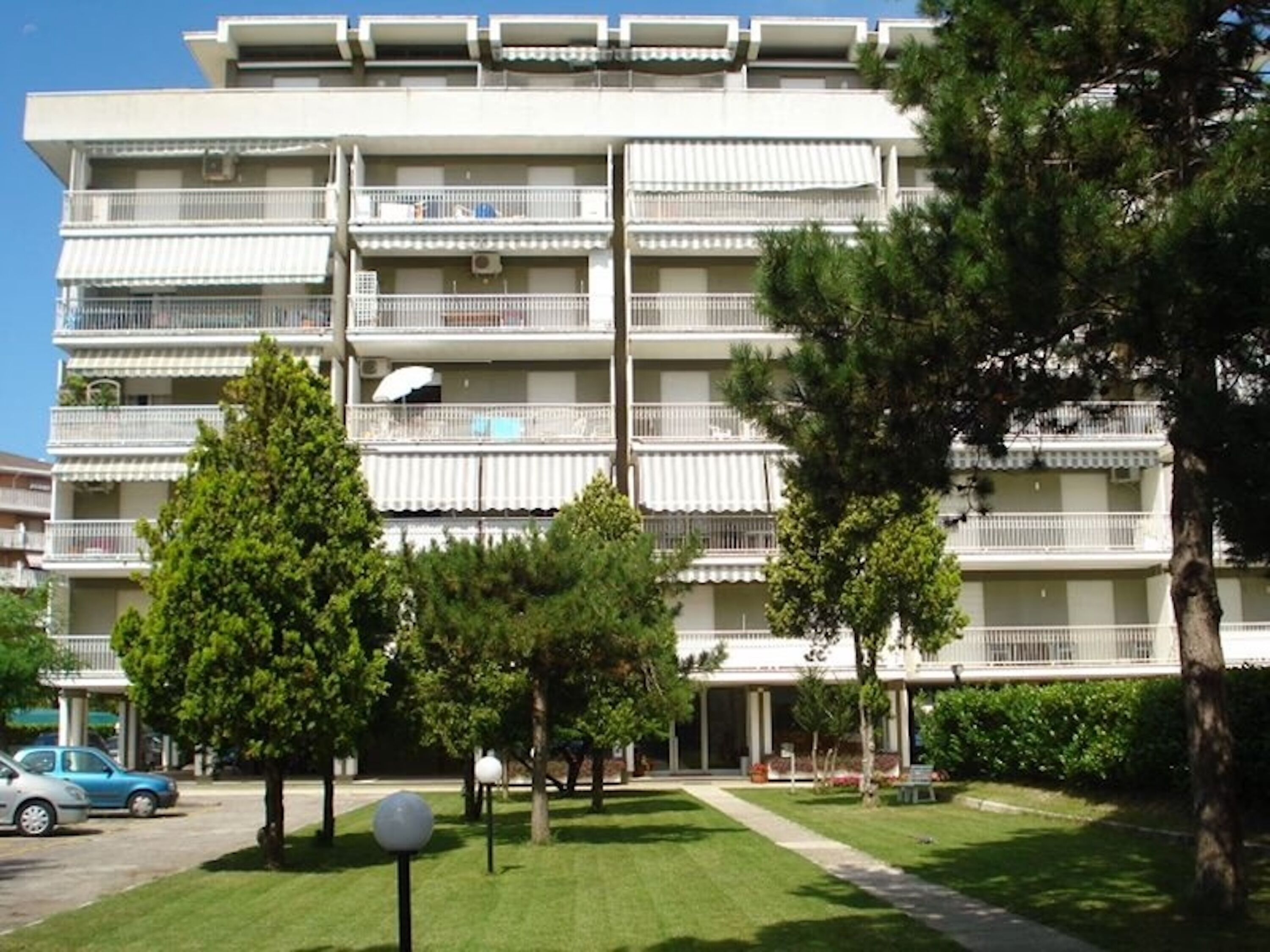 A multi-story residential building with balconies, a well-maintained lawn, and a parking area.