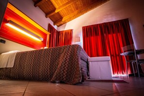 A modern hotel room with a large bed, red curtains, and a wooden ceiling.
