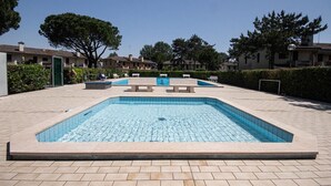 Uma piscina retangular com um deck ladrilhado, bancos e um céu azul límpido.