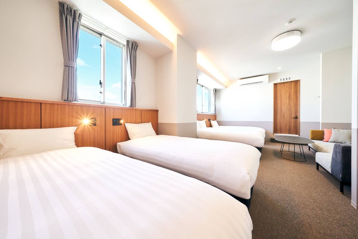 A hotel room with two beds, a desk, a chair, and a sofa.