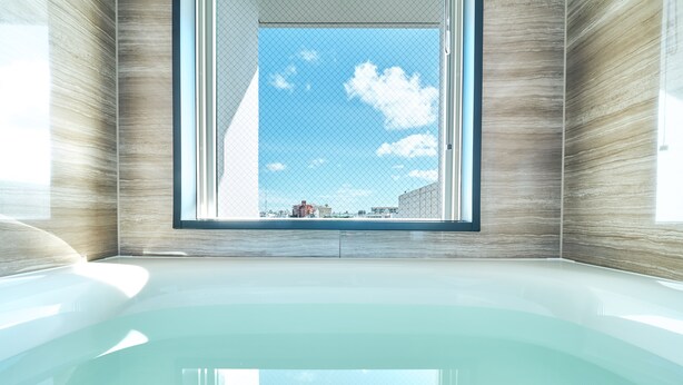 A modern bathroom with a large window, a bathtub, and a view of buildings outside. - Rakuten STAY Naha Yachimun Street (Naha)