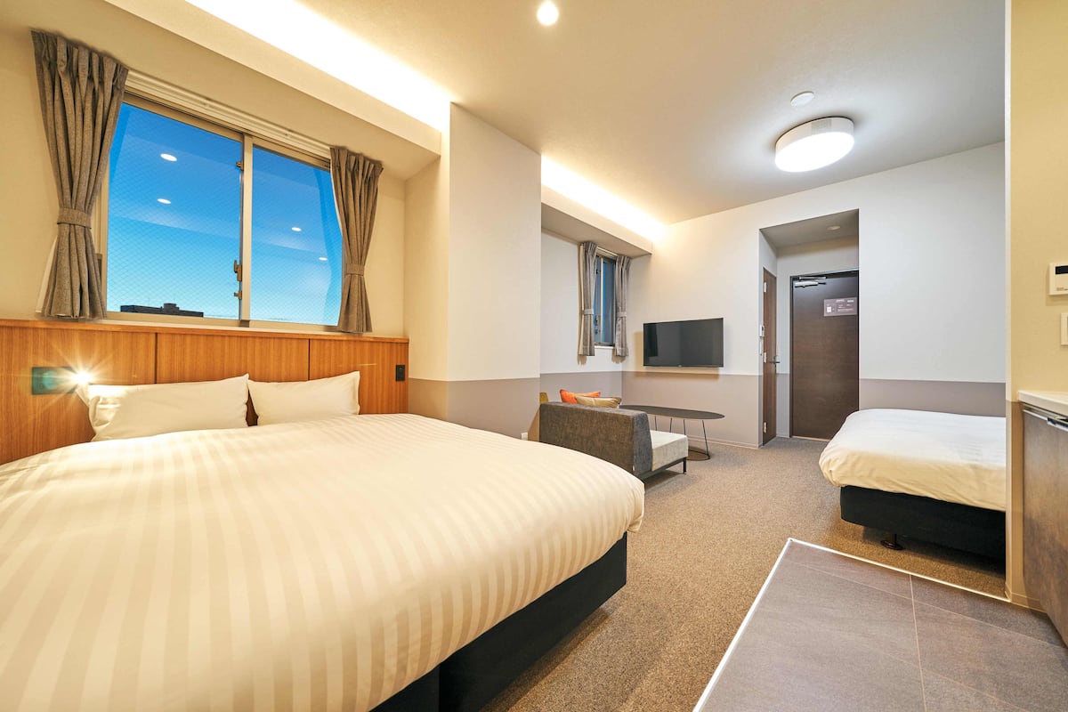A hotel room with a large bed, a smaller bed, a desk, a TV, and a bathroom door.