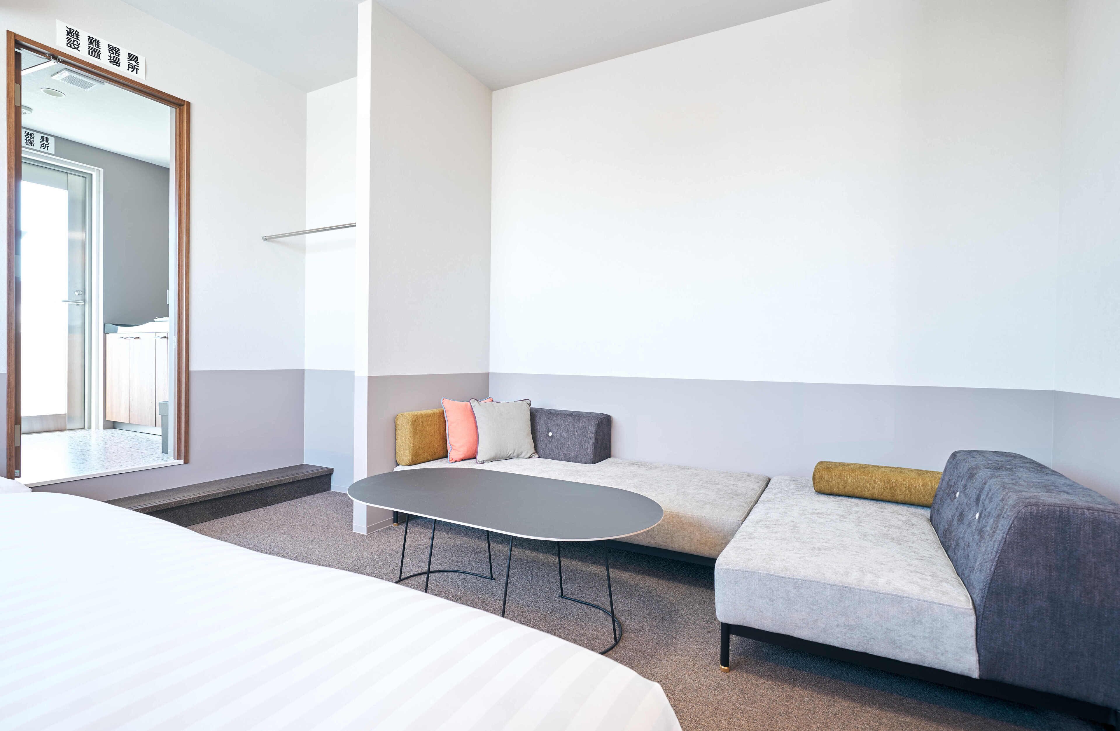 A modern hotel room with a bed, a sofa, a small table, and a mirror.