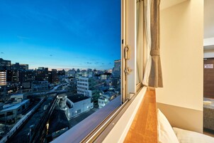 Vista da cidade a partir de uma janela de quarto de hotel, com edifícios e uma linha de trem.