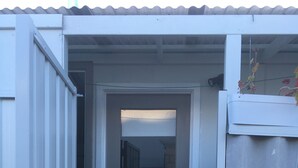 Una puerta blanca con un panel de vidrio, un escalón que lleva a la entrada y una reja metálica a la derecha.