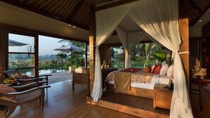 A spacious bedroom with a large bed, wooden flooring, and a view of a lush garden. - Kaba Kaba Estate (Cepaka)