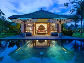 Une villa luxueuse dotée d’une grande piscine, d’une structure au toit de chaume et d’un intérieur bien éclairé.