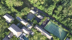 An aerial view of a resort with multiple bungalow-style accommodations, a tennis court, and a swimming pool. - Kaba Kaba Estate (Cepaka)