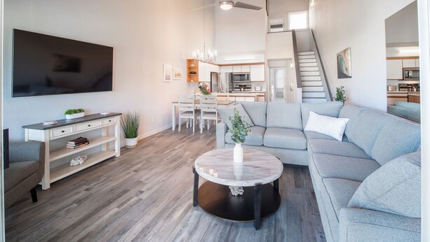 En moderne stue med et fladskærms-tv, et spiseområde, en grå sofa og en trappe, der fører til en etage over.