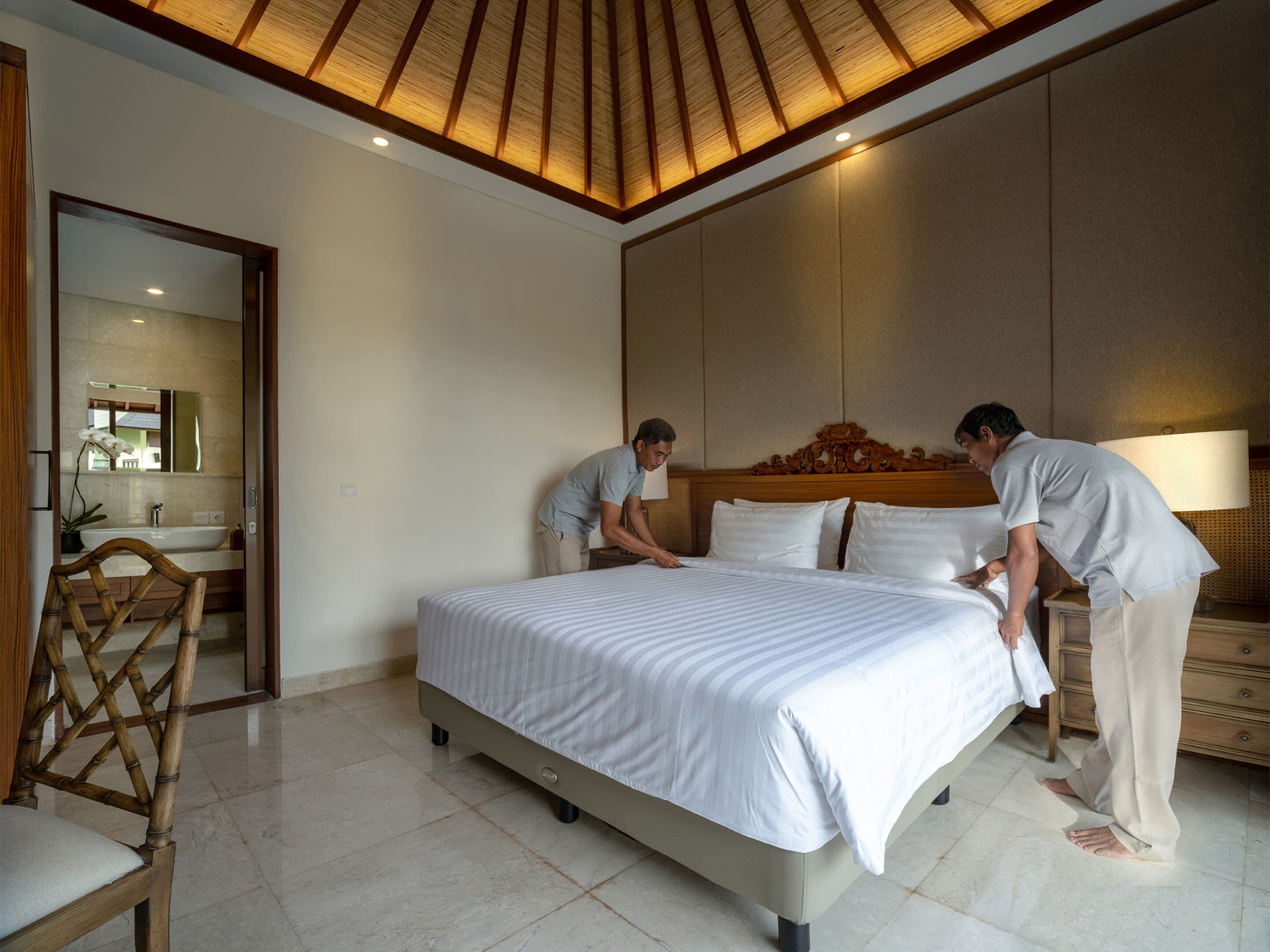 Camera d'albergo moderna con un grande letto, una testiera in legno, un comodino con una lampada e un bagno visibile attraverso una porta aperta.