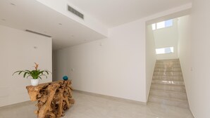 Un interior espacioso y moderno con una consola de madera, una planta en maceta y una escalera que conduce a un nivel superior.
