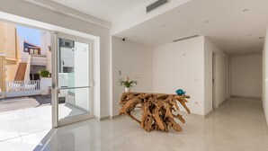 Un interior moderno con una puerta de cristal que da a un espacio exterior, una consola de madera y un suelo de baldosas impecable.