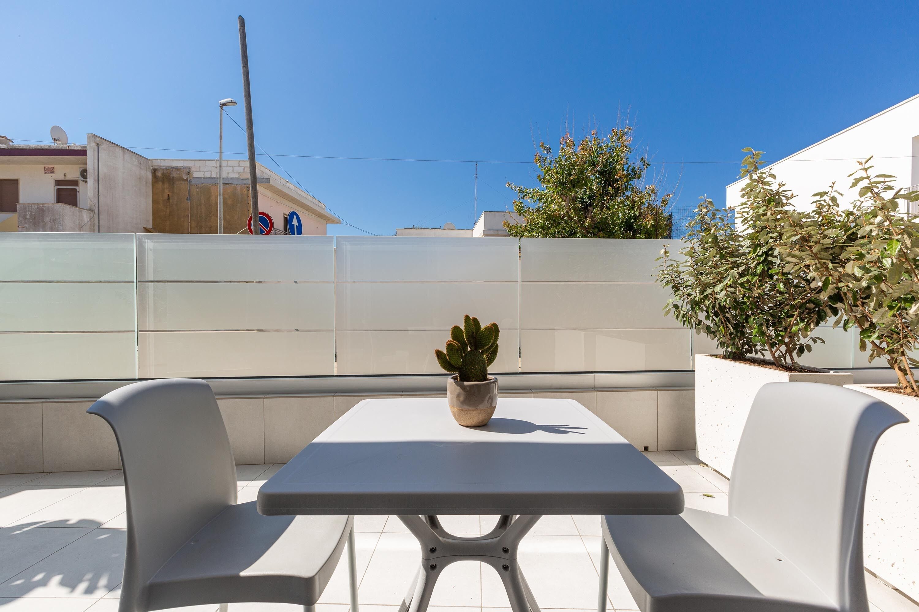 A balcony with a table and two chairs, a potted cactus, and a white wall with a satellite dish.