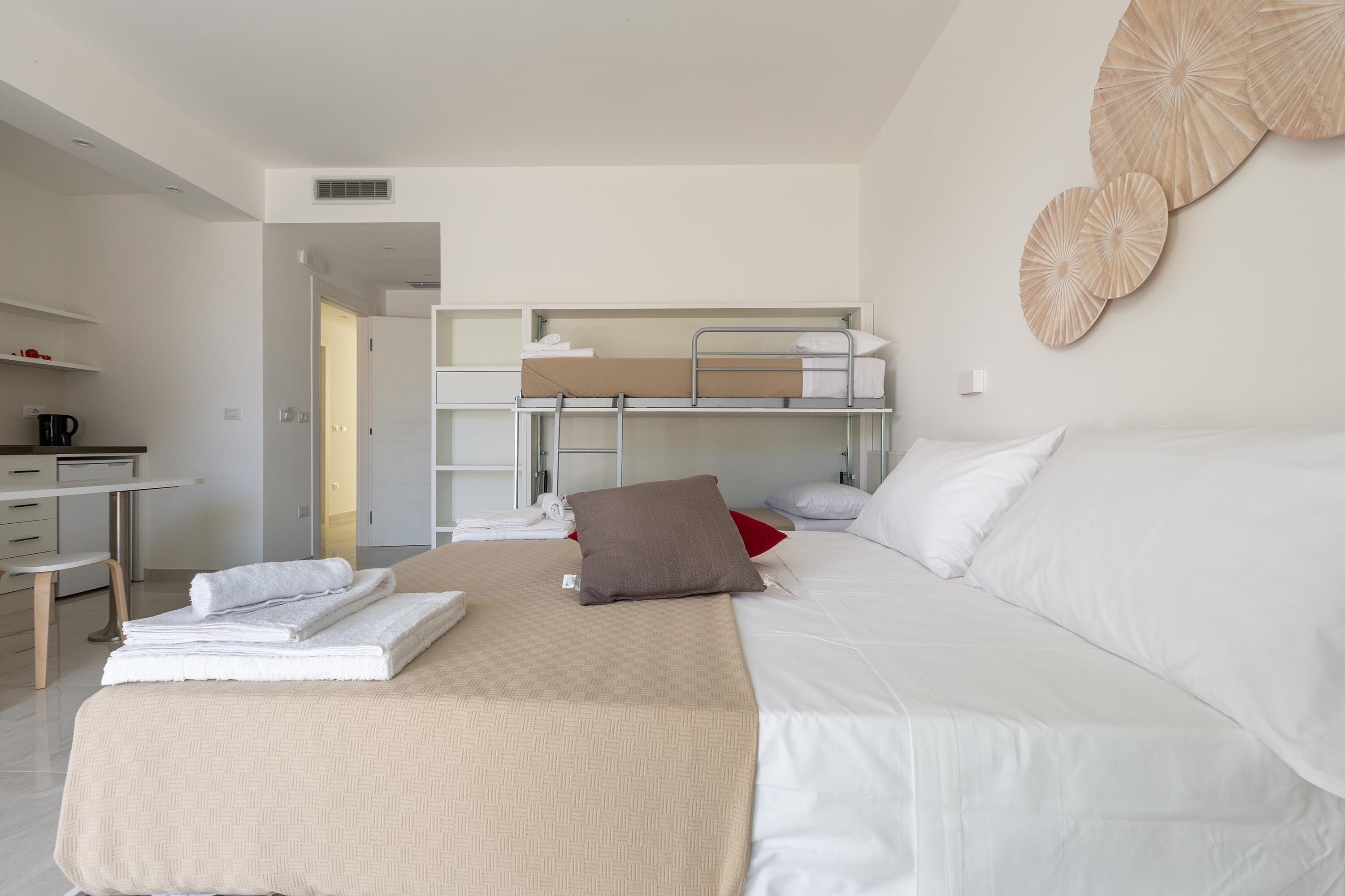A modern hotel room with a bunk bed, a desk, and a large bed.