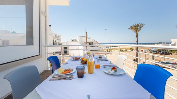 Una mesa de comedor preparada con platos, cubiertos y bebidas en un balcón con vistas a un cielo despejado y un aparcamiento.